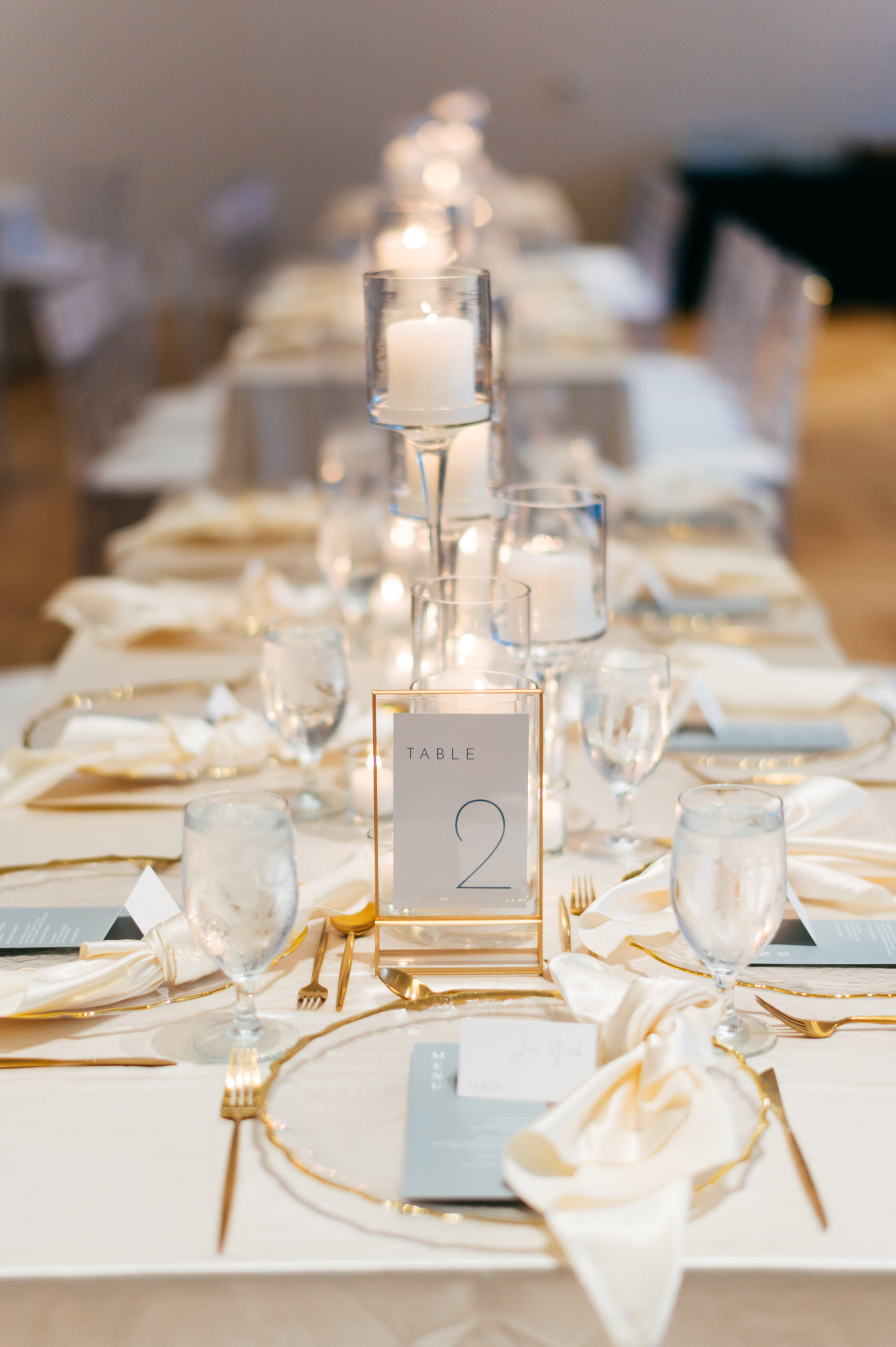 Neutral Modern Long Wedding Reception Feasting Tables with Gold Flatware and Gold Rimmed Chargers | Modern Gold Frame Table Numbers | Ybor Rental Kate Ryan Event Rentals