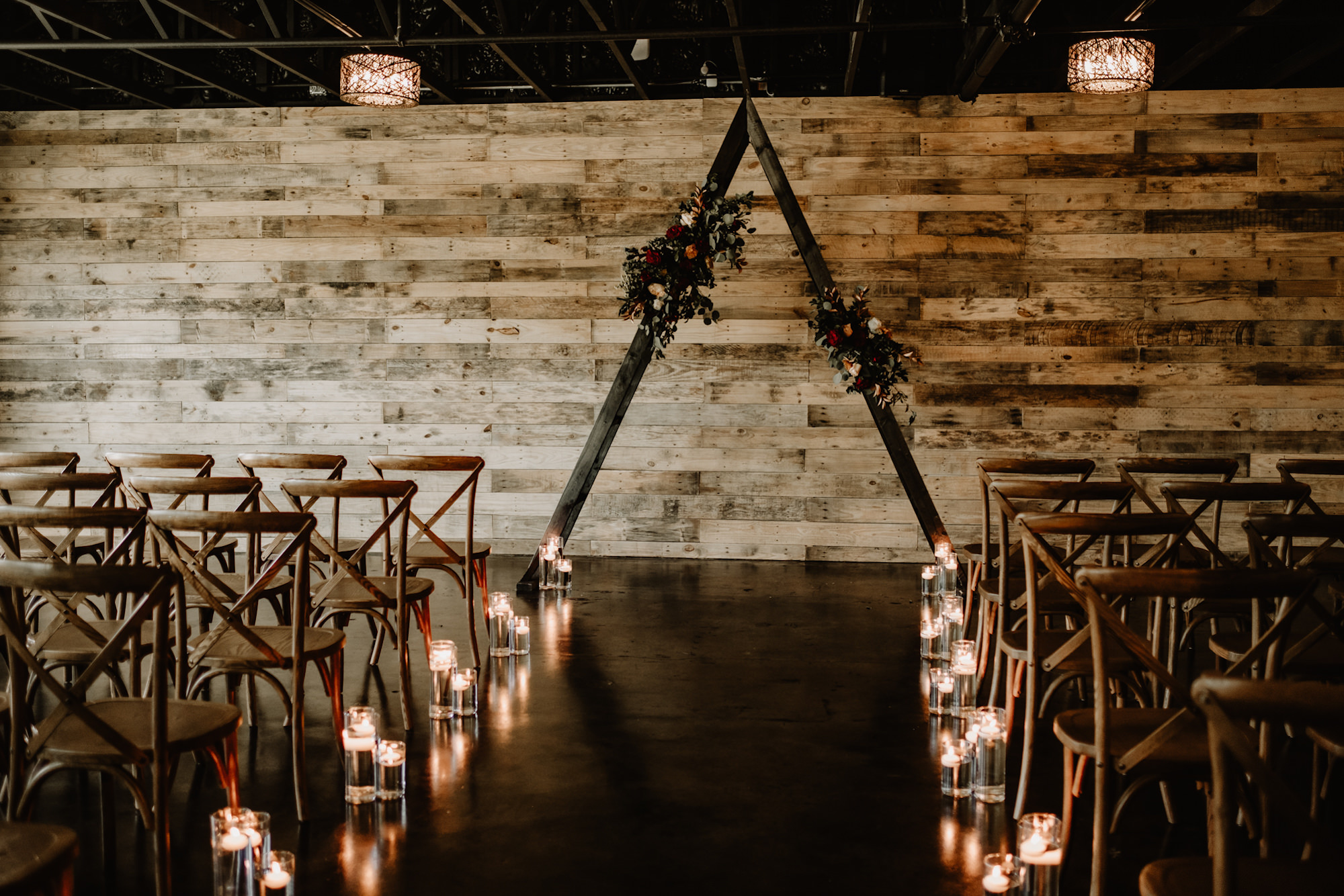 Triangle Ceremony Arch with Maroon, Cream, and Orange Flowers | Candle Lit Aisle Decor Inspiration | Indoor Ceremony Pallet Wood Wall | Tampa Bay Wedding Venue The West Events