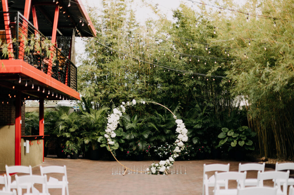Simple Classic Outdoor Bamboo Courtyard Wedding Decor, Hanging Bistro Lights, Round Circular Gold Metal Arch with Lush White and Greenery Flowers | St. Pete Wedding Florist Save the Date Florist | Wedding Venue NOVA 535