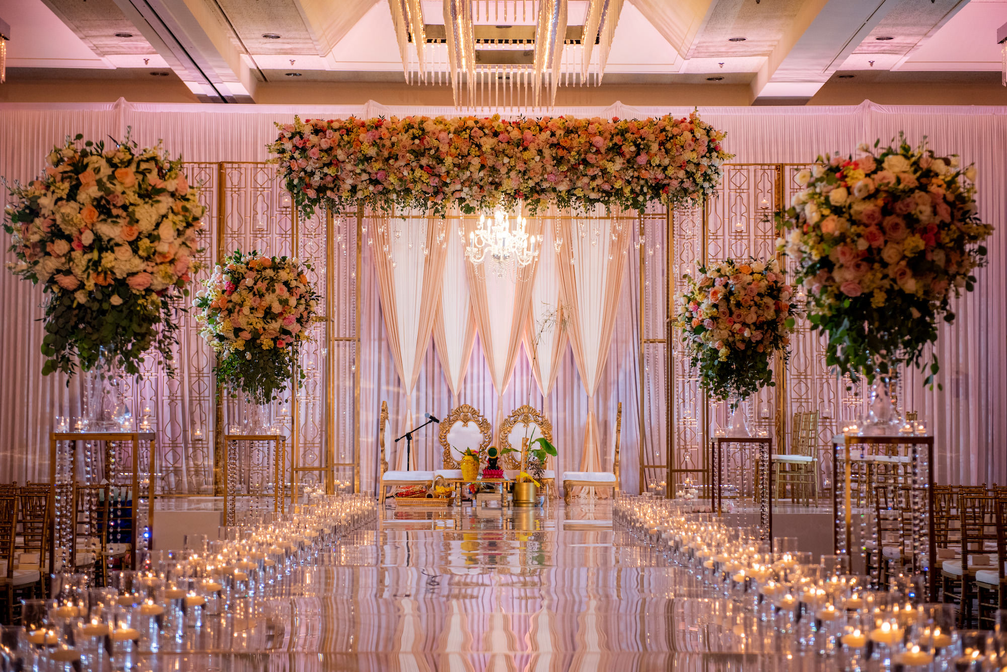 Luxurious Ballroom Wedding Ceremony, Indian Altar with Ornate Gold Chairs and Chandelier, Lush Floral Arrangements with Blush Pink and White Flowers, Candlelight Path Down Aisle | Tampa Bay Wedding Venue Hilton Downtown Tampa