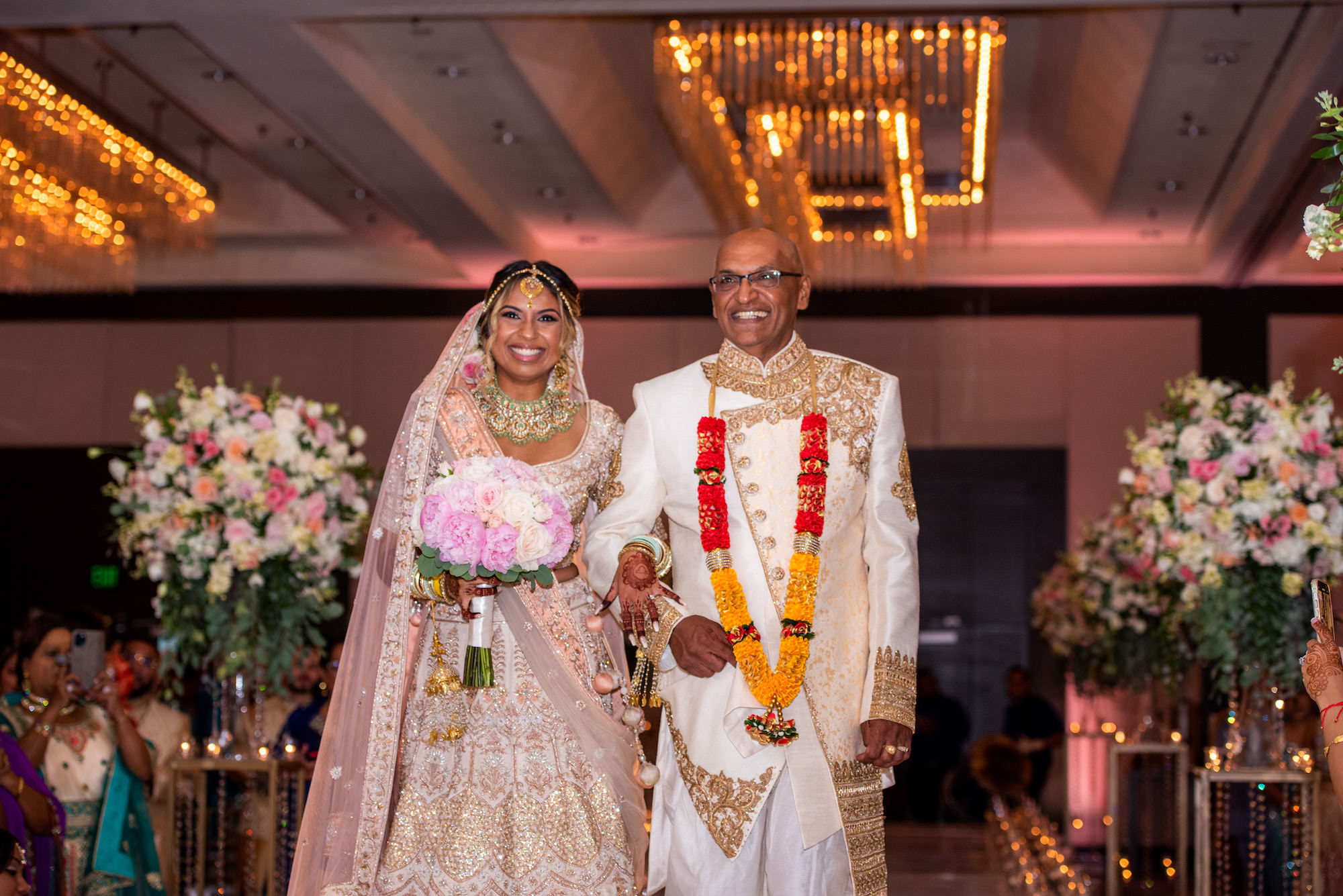 Elegant Bride Walks Down Aisle With Father During Traditional Indian Wedding Ceremony, Bride in Modern Saree With Gold and Ivory Detailing, Head Piece Jewelry, Holding Blush Pink Floral Bouquet | Florida Wedding Venue Hilton Downtown Tampa