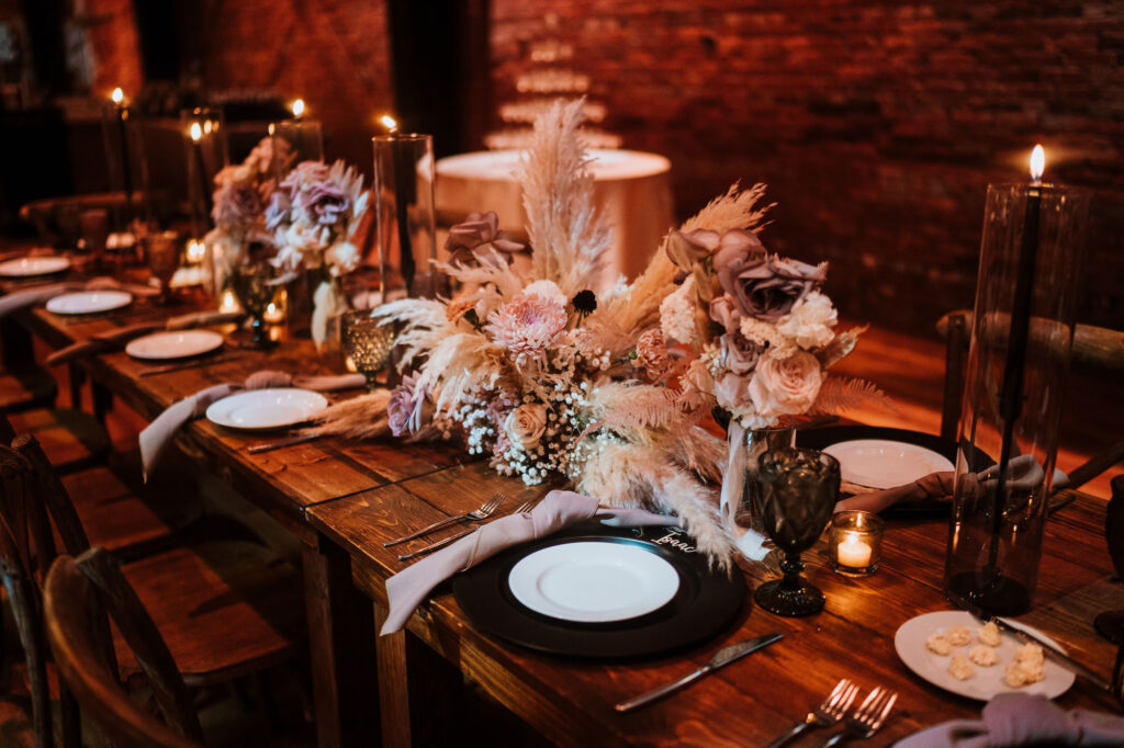 Dark and Moody Tablescape with Pampas Leaf Centerpieces, Mauve Florals, Black Chargers, White Plates on Wooden Tables Reception Ideas