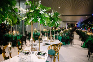Modern Glam Gold and White Serpentine Table with Louis Pop Chairs and Velvet Cushions | Tall Gold Flower Stand with Monstera, White Stock Flowers | Emerald Green and Black Wedding Inspiration | Tampa Bay Florist FH Events | A Chair Affair