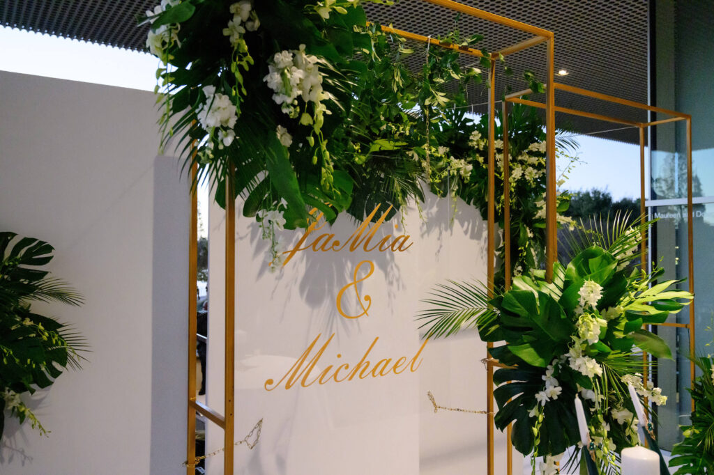 Acrylic Personalized Wedding Sign with Gold Lettering | Gold Altar Inspiration | Tropical Floral Arrangements with Monstera, Palm Leaf, and White Stock Flowers