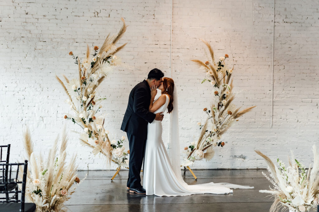 Bride and Groom First Look Wedding Portrait | Indoor Wedding Ceremony | Asymmetrical Round Boho Arch with Boho Pampas Grass White Palm Frond Floral Arrangements | Lakeland Industrial Wedding Venue with White Brick Walls Haus 820