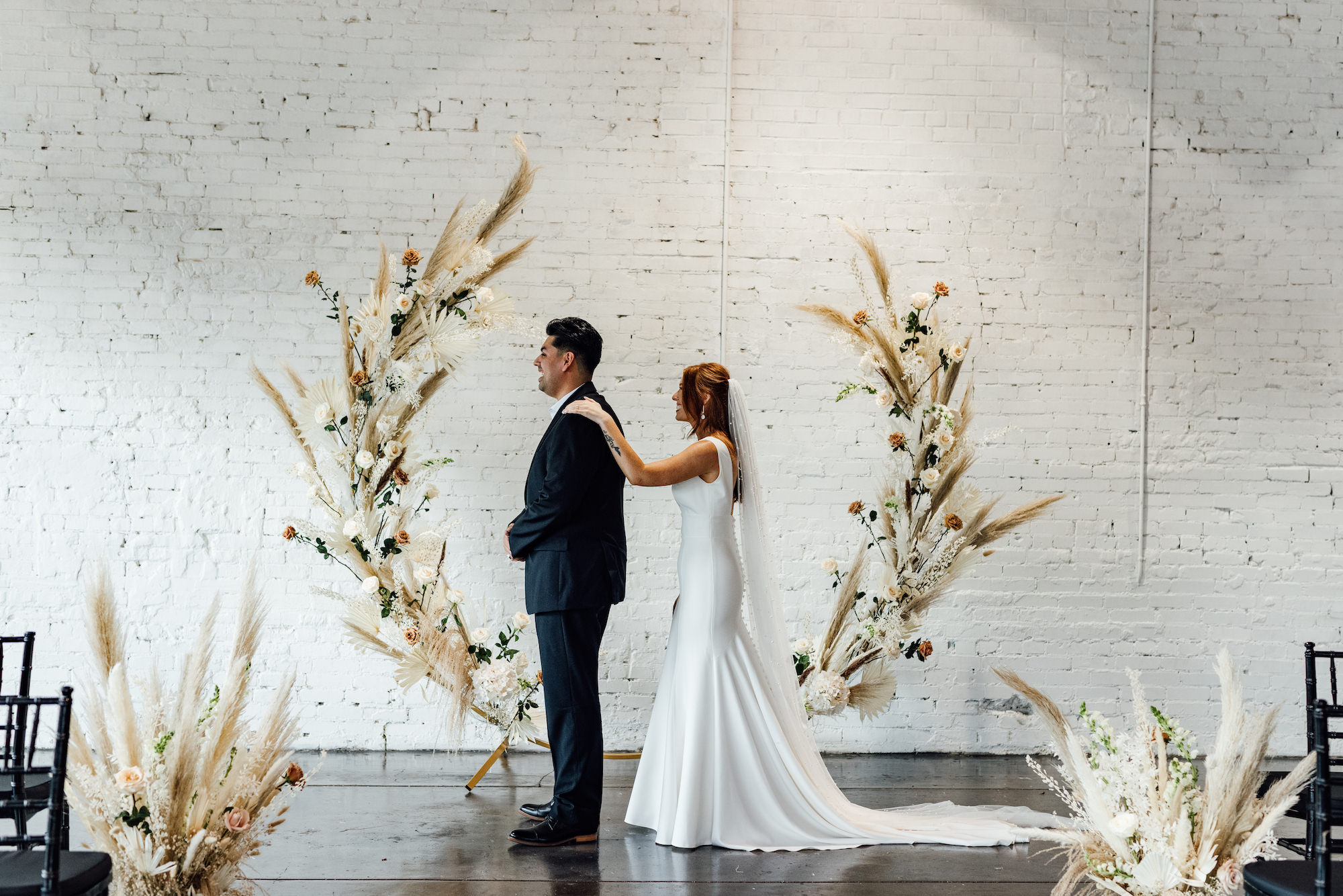 Bride and Groom First Look Wedding Portrait | Indoor Wedding Ceremony | Asymmetrical Round Boho Arch with Boho Pampas Grass White Palm Frond Floral Arrangements | Lakeland Industrial Wedding Venue with White Brick Walls Haus 820