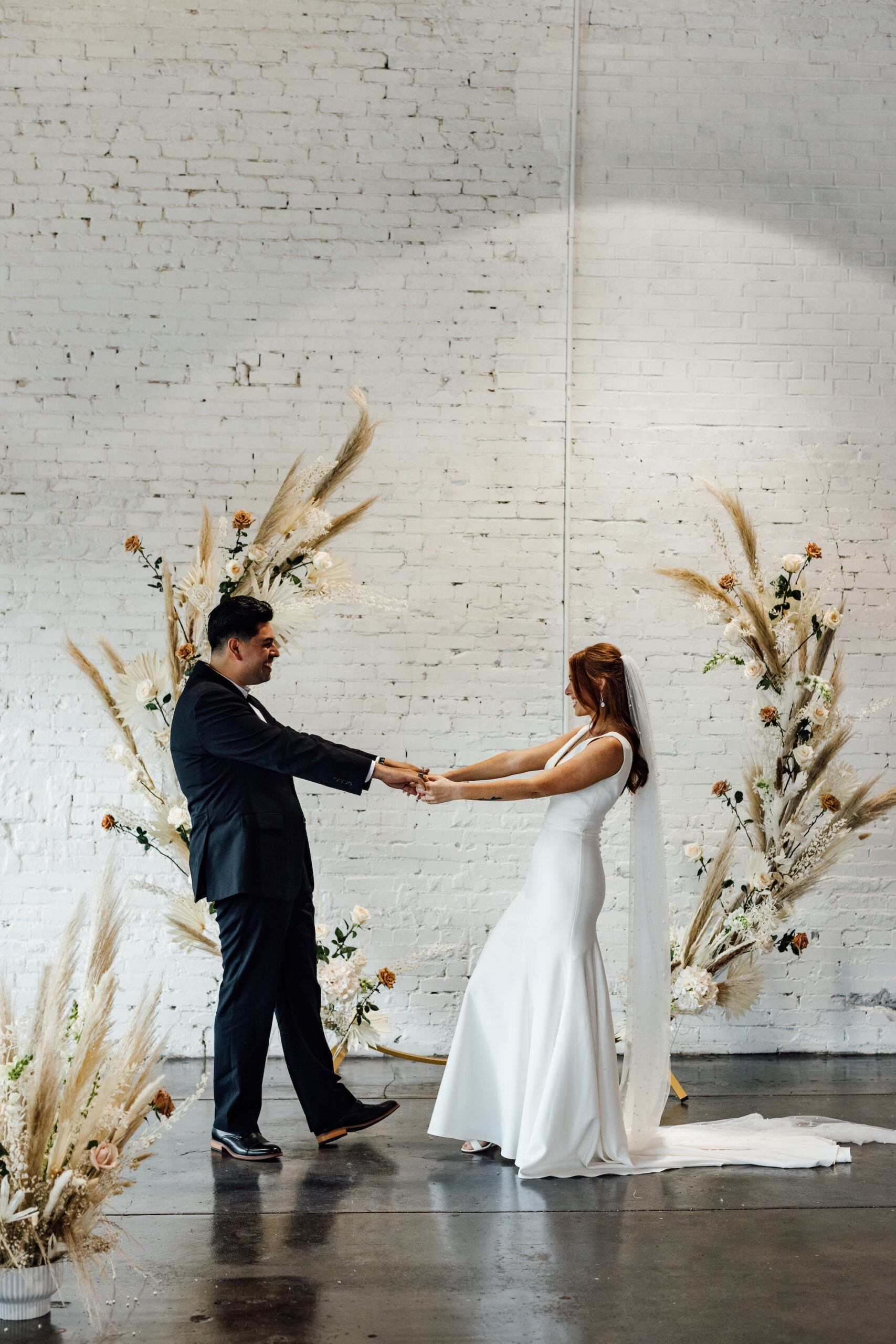 Bride and Groom First Look Wedding Portrait | Indoor Wedding Ceremony | Asymmetrical Round Boho Arch with Boho Pampas Grass White Palm Frond Floral Arrangements | Lakeland Industrial Wedding Venue with White Brick Walls Haus 820