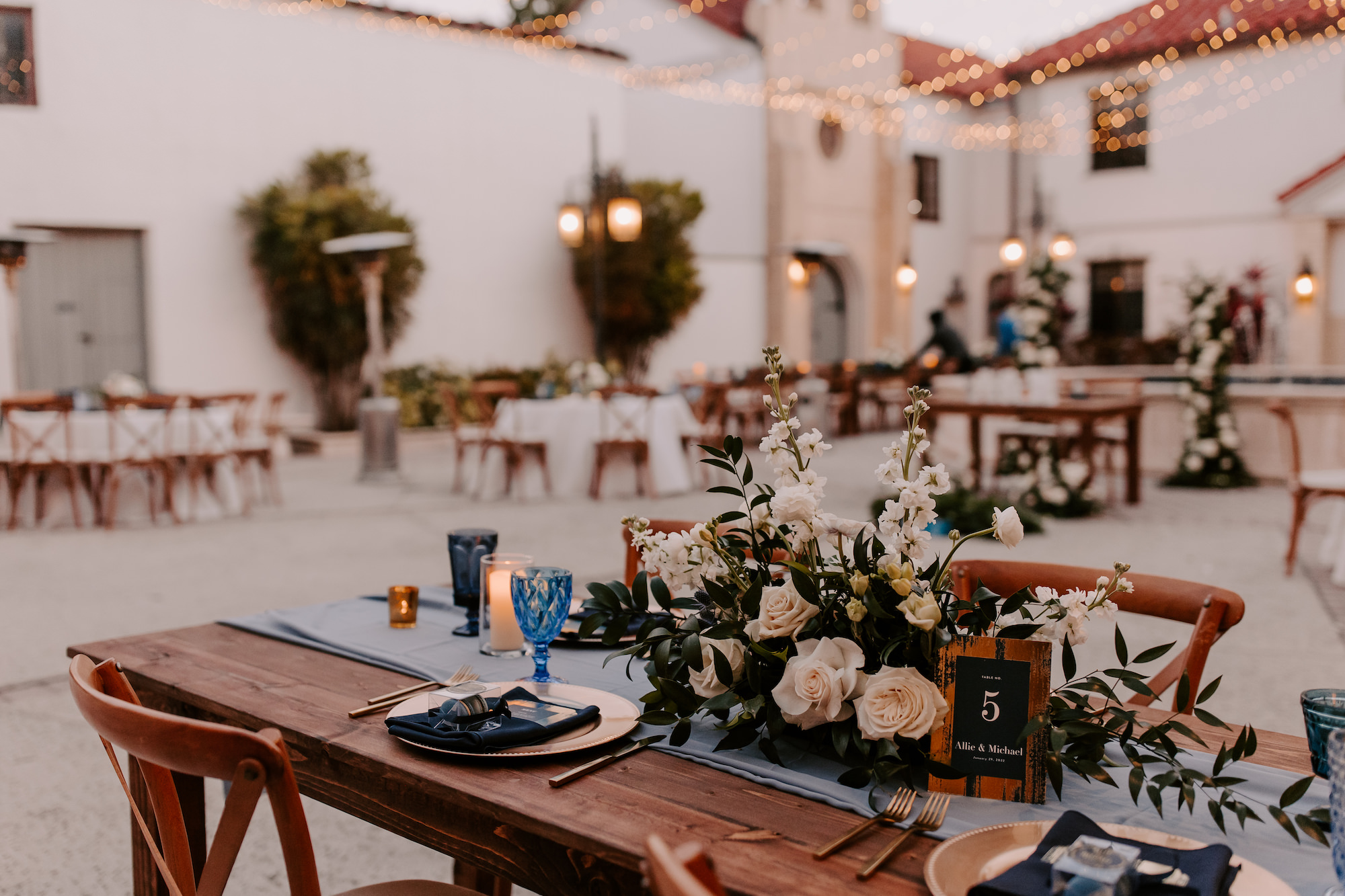 Romantic French Country Outdoor Courtyard Inspiration | White Ranunculus, Dendrobium, Rose, and Ruscus Greenery Centerpiece Ideas | Dusty Blue Wedding Reception Decor Inspiration | Sarasota Wedding Planner Coastal Coordinating