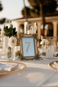 Classic Gold Mirror Table Number Inspiration with White Gerpom and Greenery with White Pillar Candles and Glass Vase Centerpieces