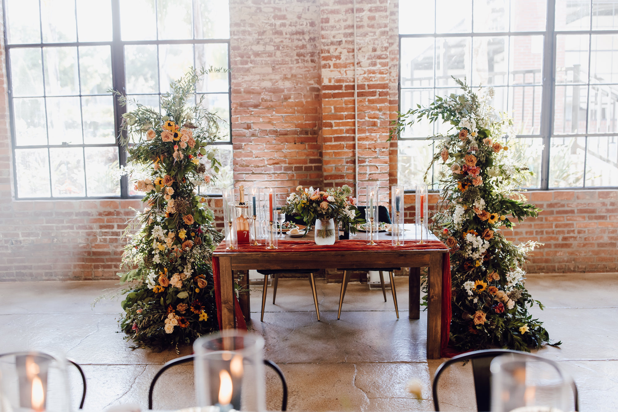 Sweetheart Head Wedding Reception Table Decor | Hurricane and Taper Candles | Boho Yellow, Orange, and White Flower Column with Greenery Inspiration | Dade City Planner Special Moments Event Planning | Venue at The Block