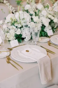 Romantic Wedding Place Setting with White China Chargers, Gold Flatware, and Floral Centerpieces | Reception Tablescape Ideas