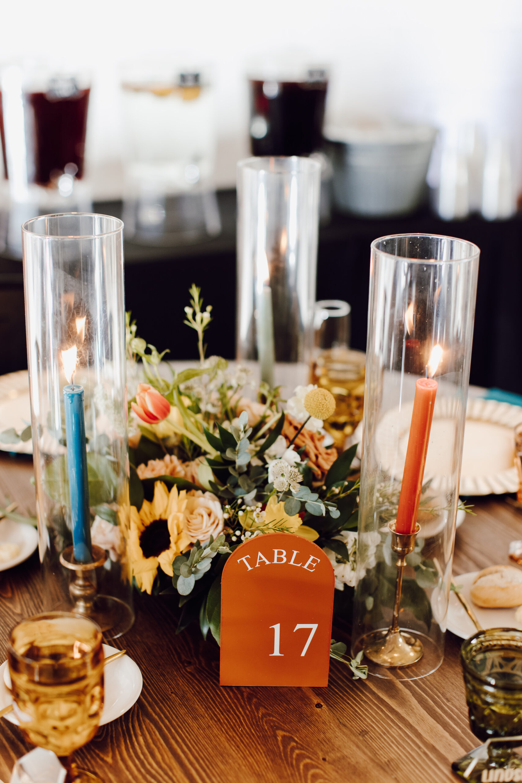 Arch Acrylic Table Numbers | Hurricane Candles with Orange and Blue Taper Candles | Sunflower, Roses, and Greenery Centerpieces Boho Wedding Reception Table Decor Ideas