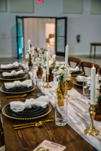 Amber Flower Vases with White Roses and Baby's Breath Wedding Reception Table Centerpiece Inspiration | Flameless White Taper Candle with Gold Holders | Black Plates with Gold Beaded Chargers and Flatware Ideas