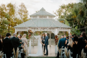 Bride and Groom Exchange Vows Under Outdoor Wedding Ceremony with White Palapa and White Folding Chairs | Florida Florist Beneva Flowers | Truly Forever Bridal