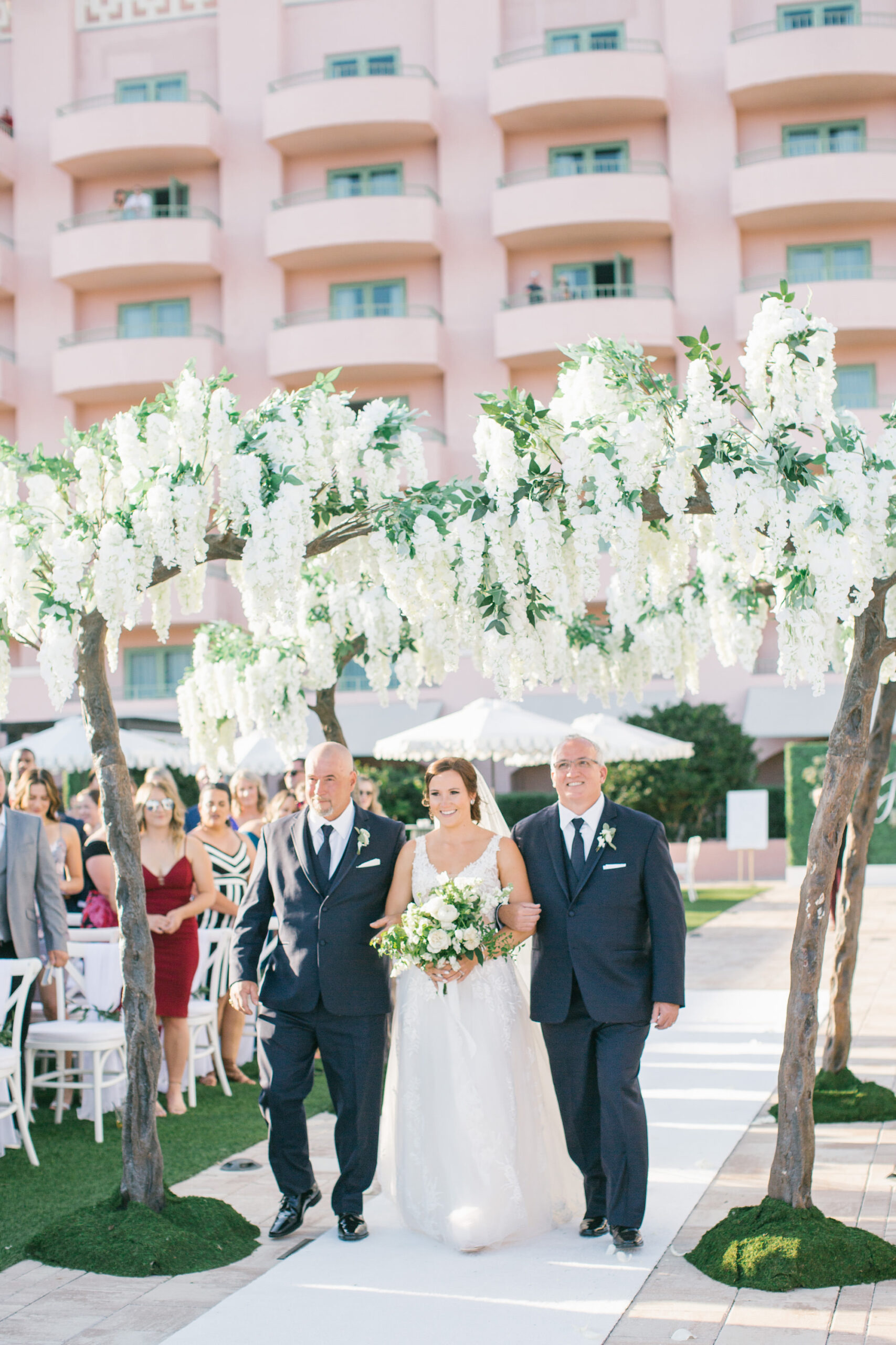 Bride and Fathers Walking Down Aisle | White Aisle Runner Inspiration | Tall Wisteria Tree Decor | Outdoor Beach Wedding Ceremony