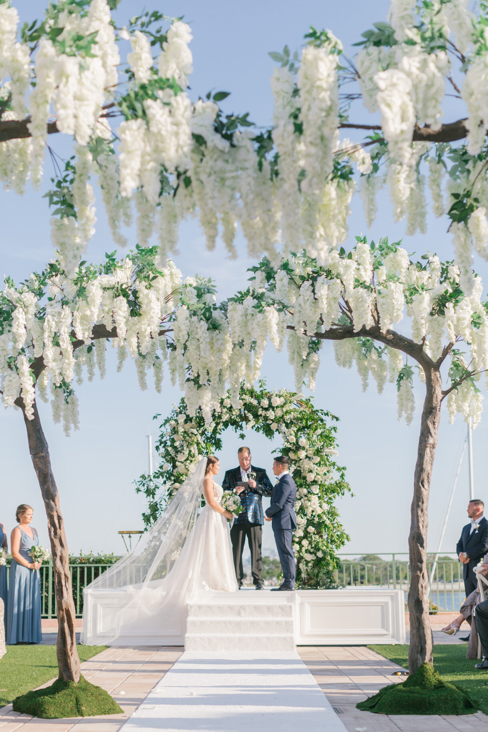 Tall Wisteria Tree Wedding Aisle Decor | Whimsical White and Greenery Garden Floral Wedding Arch with White Aisle Runner | Downtown St. Pete Venue The Vinoy | Planner Parties a La Carte | Videographer Mars the Moon Films
