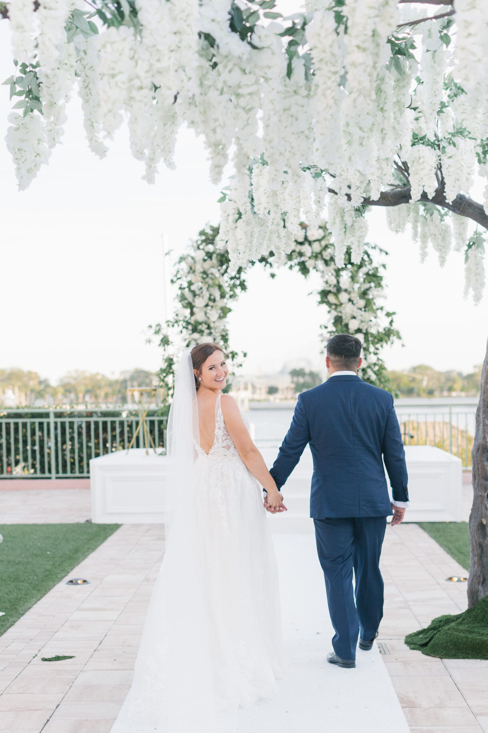 Tall Wisteria Tree Wedding Ceremony Aisle Decor | Whimsical White and Greenery Garden Floral Wedding Arch with White Aisle Runner