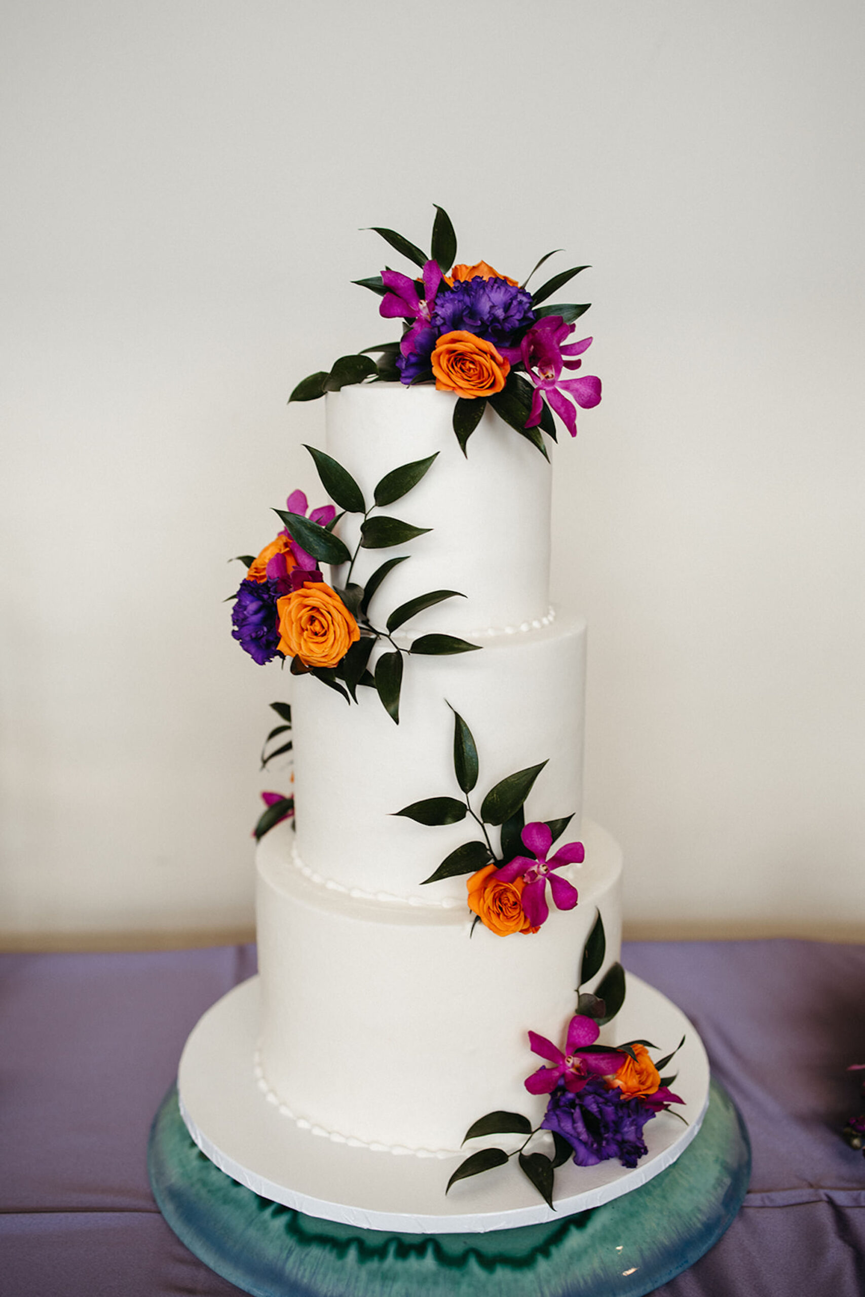 White Three-tiered Wedding Cake with Real Orange, Fuchsia, and Violet Flowers and Greenery Ideas