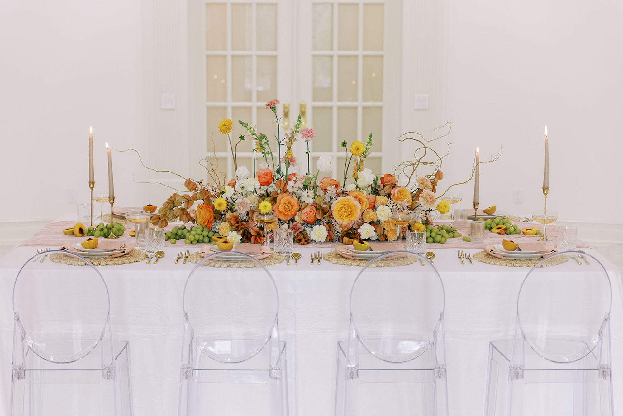 Romantic, Spring-Inspired White, Orange, Yellow, Peach Rose, Dahlias, and Carnation Centerpiece Ideas | Taper Candle with Gold Holder Wedding Reception Inspiration | Ghost Chair Seating