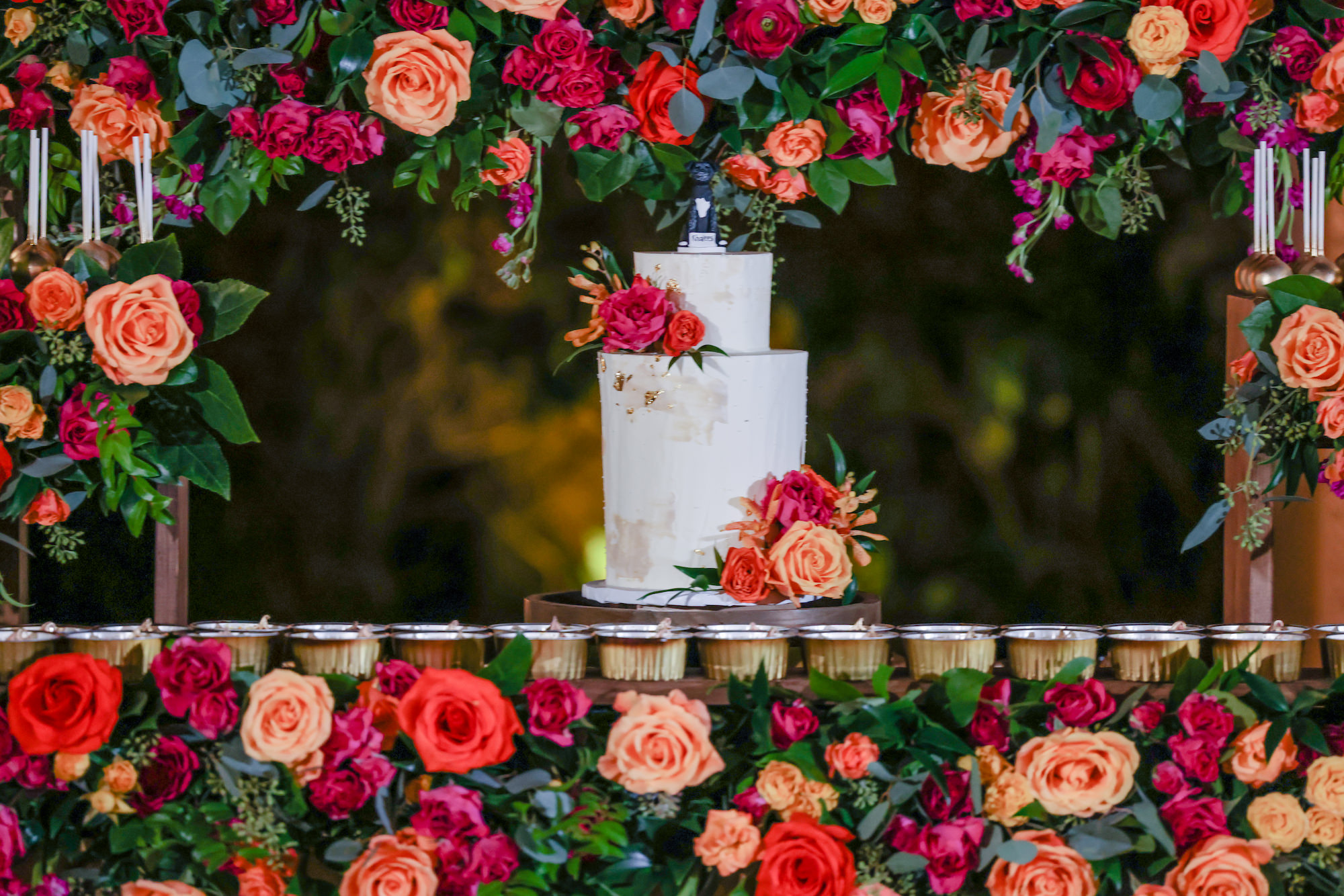 Two-Tiered Semi-Naked Wedding Cake | Tropical Maroon Carnations, Orange, Pink and Red Roses with Eucalyptus and Ruscus Greenery Dessert Table Floral Arrangement Inspiration | St. Pete Bakery The Artistic Whisk
