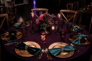 Gold Chargers and Emerald Green Napkins on Deep Purple Linen Dark and Moody Jewel Toned Wedding Reception Place Setting Inspiration