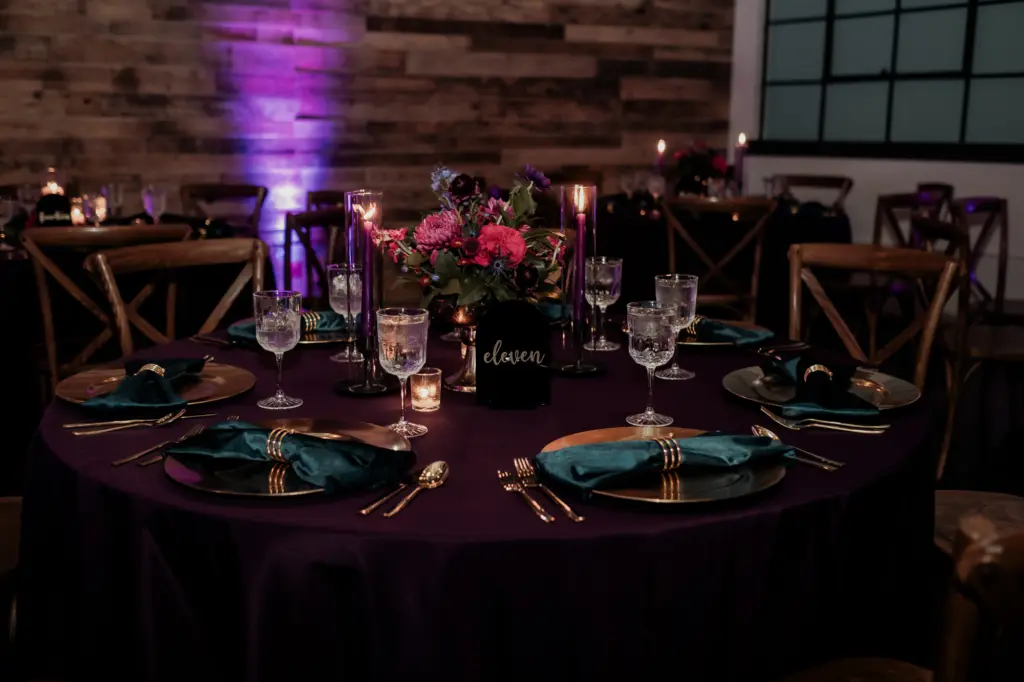 Gold Chargers and Emerald Napkins on Deep Purple Linen with Pink Centerpieces | Dark and Moody Wedding Reception Place Setting Inspiration