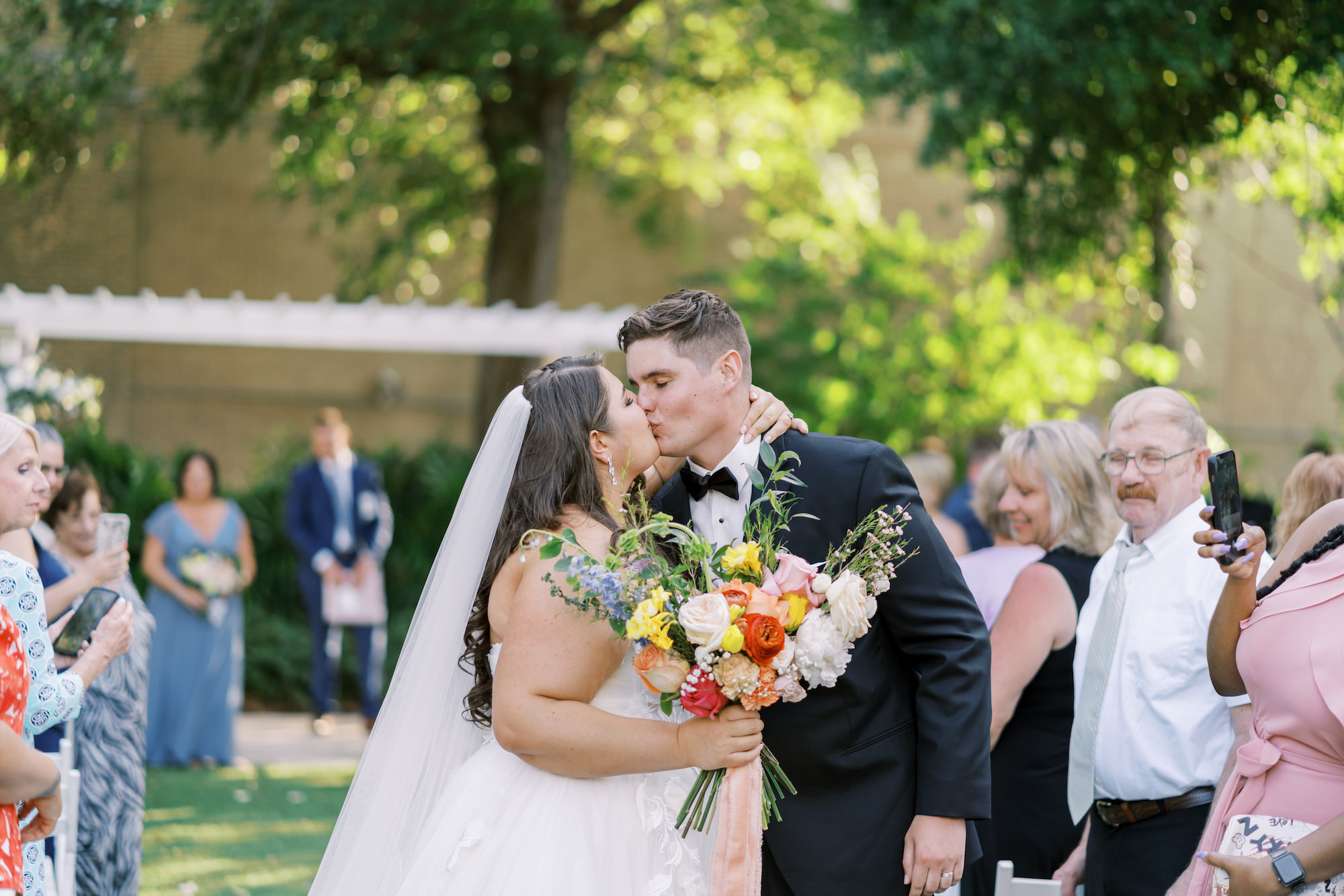 Bride and Groom Wedding Aisle Kiss | Spring Bridal Bouquet with Roses, Carnations, Snapdragons, and Greenery Ideas