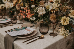 Wedding Tablescape with Florals and Greenery, White Linen, Gray Napkins, Black Glassware and Cream Chargers