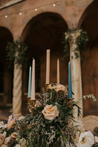 Tapered Candle Wedding Centerpiece in Muted Rainbow Colors Surrounded by Florals and Greenery