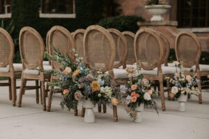 Rustic Boho Wooden Chairs with Muted Rainbow Floral Wedding Aisle Decor | Whimsical Boho Wedding Decor with Multi Colored Candles and Muted Pastel Wedding Florals and Beige Sheer Linen | Ceremony Seating Decor Ideas