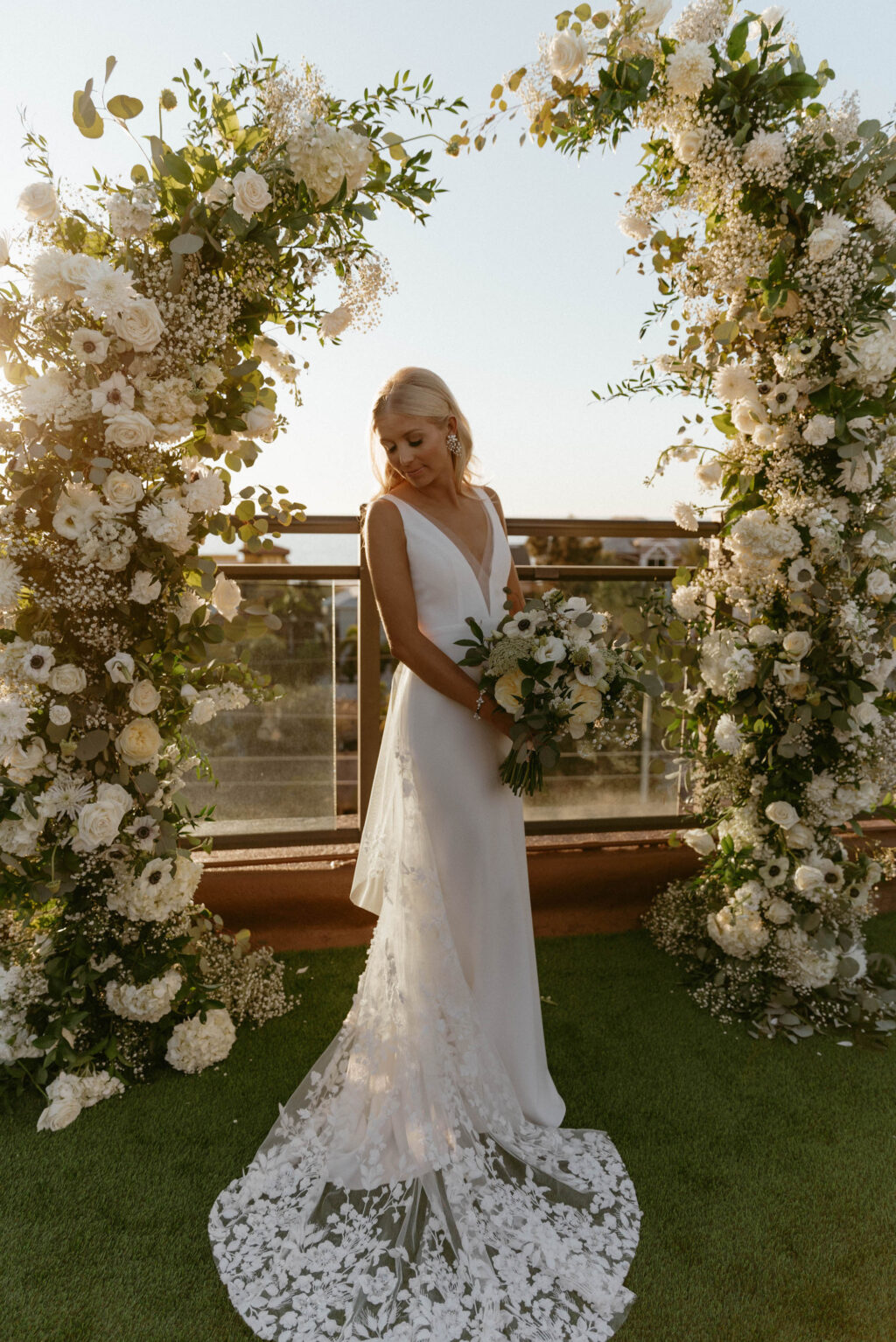 Bride in Illusion Lace Back Wedding Dress Golden Hour Wedding Portrait in Front of Floral Ceremony Arch Inspiration and Beachy White and Cream Bridal Bouquet with Greenery Details | St. Pete Beach Lemon Drops Weddings & Events
