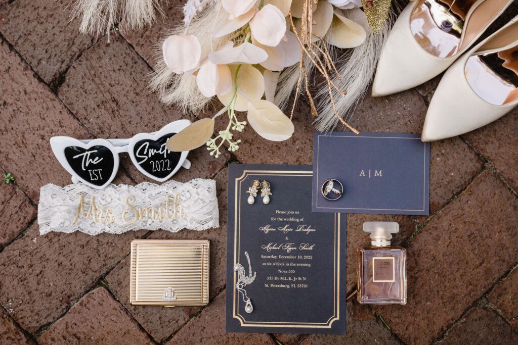 Black and Gold Wedding Invitation Inspiration Flatlay with White Bridal Sunglasses, Lace Garter and Dried Floral Details