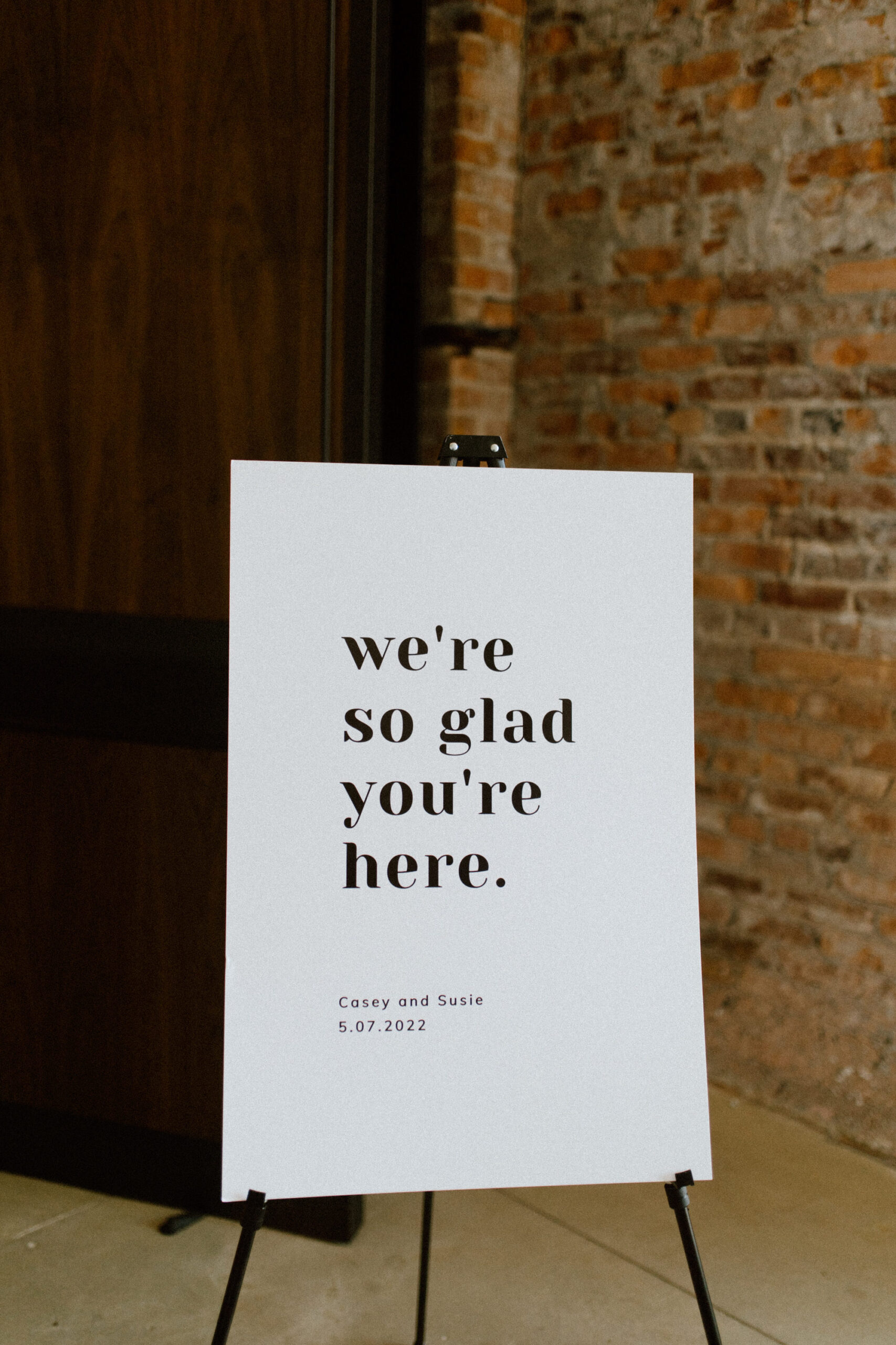 Modern "We're So Glad You're Here" Wedding Welcome Ceremony Sign in Classic Black and White