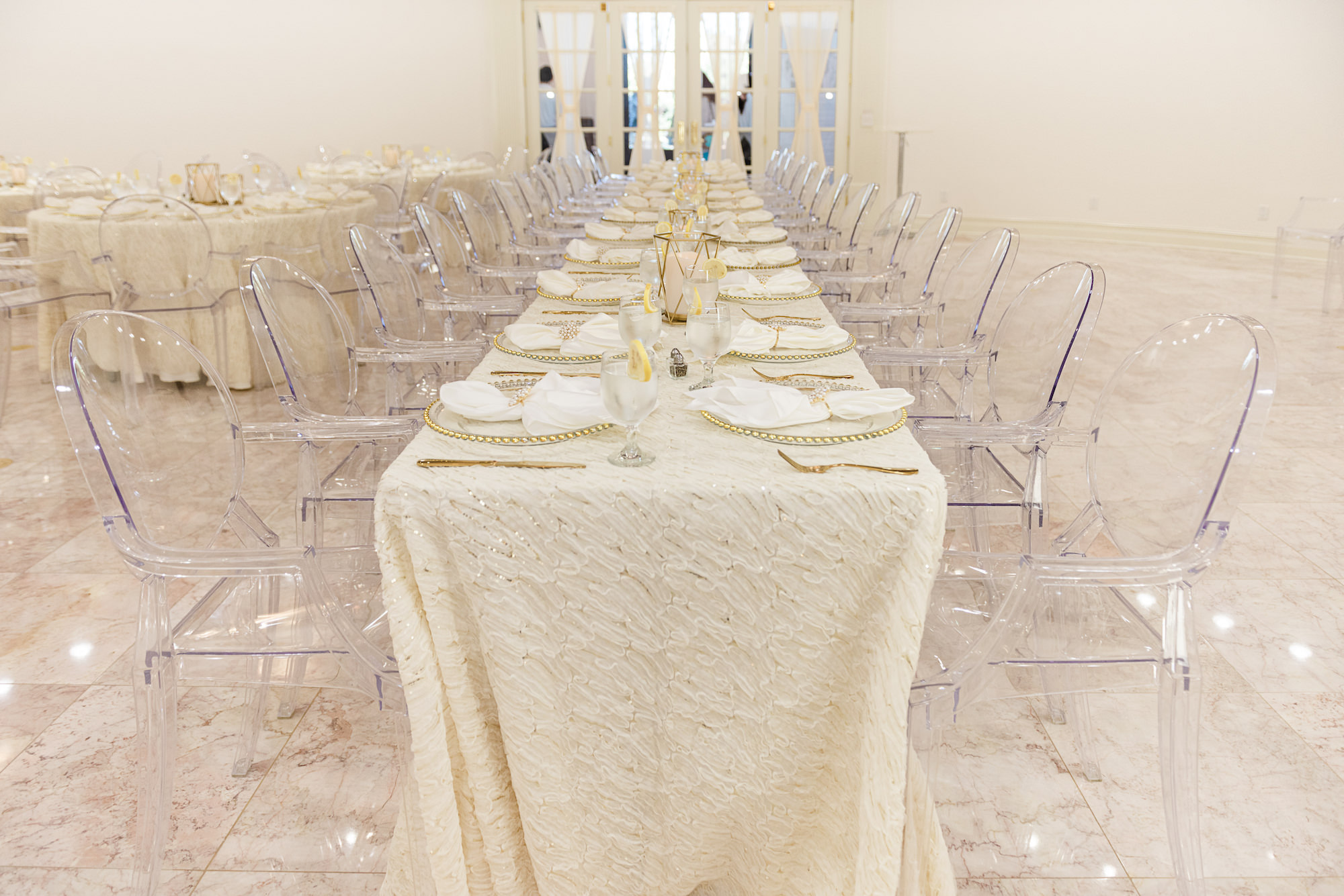 Elegant Long Feasting Tables with White Linens and Ghost Chairs Inspiration | Gold Beveled Glass Chargers and Votives | Tampa Bay Outside the Box Rentals | Whitehurst Gallery