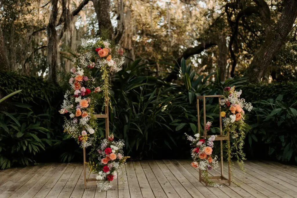Gold Stand Holding Orange, Red and Pink Florals as Arch Wedding Ceremony Decor in Garden Inspired Wedding | Tampa Wedding Venue Mill Pond Estates