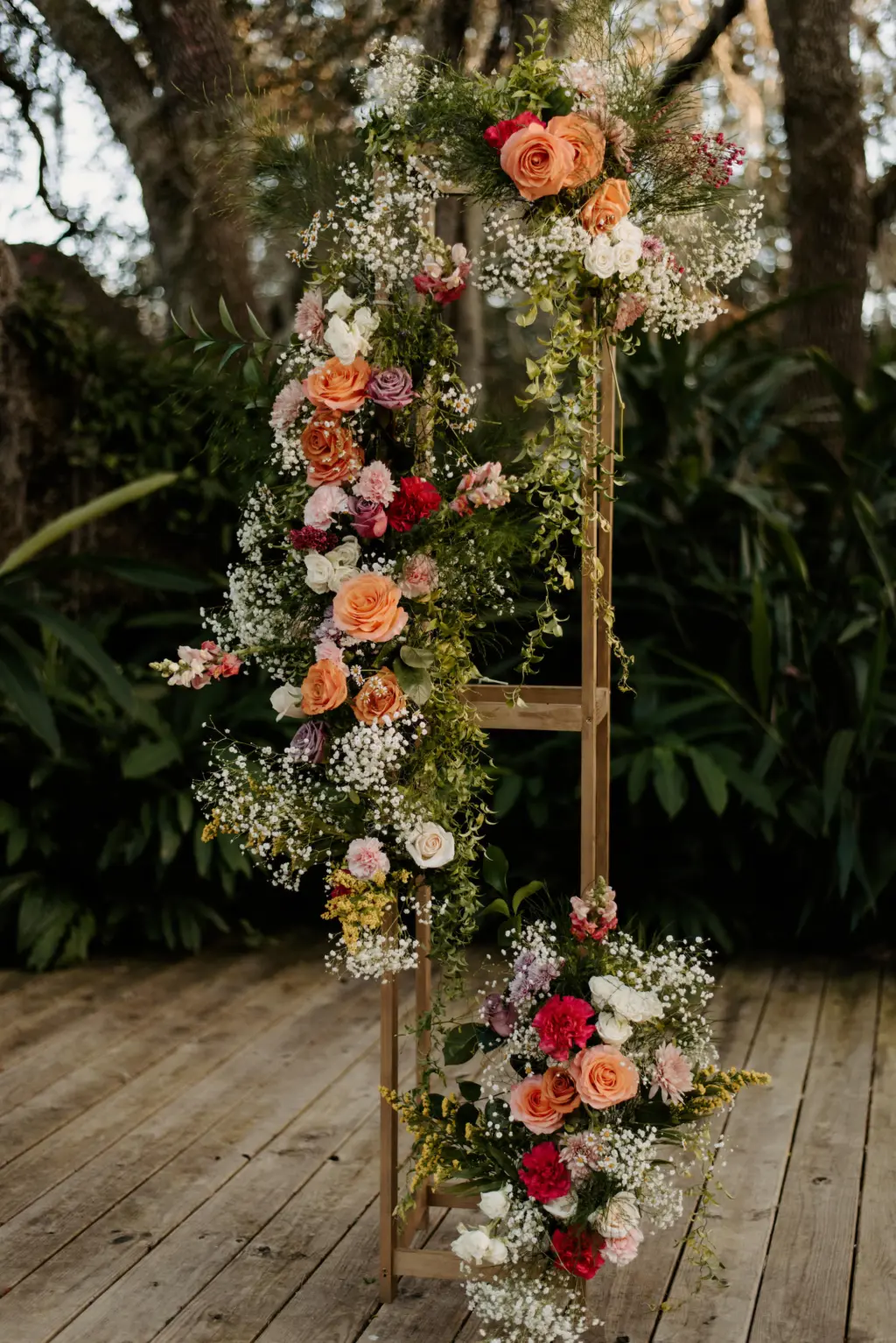 Gold Stand Holding Orange, Red and Pink Florals as Arch Wedding Ceremony Decor in Garden Inspired Wedding