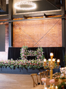 Industrial Wedding Reception Inspiration | Bridal Party Black Feasting Table with Extravagant Flower Arrangements | Pink, White, and Yellow Roses with Eucalyptus Greenery