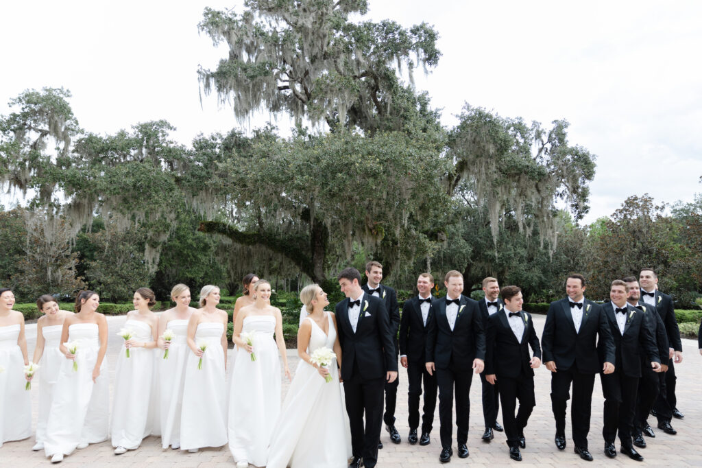Groom and Groomsman Black Tuxedo Classic Wedding Attire Inspiration | All-White Amsale Bella Bridesmaids Strapless Dress Ideas with Classic Cala Lily Bouquets
