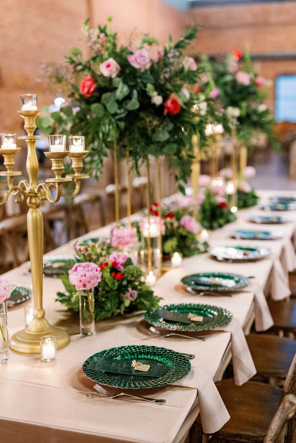 Gold Candelabra | Pink, Red, and White Roses with Eucalyptus Greenery in Gold Tall Stands | Green Chargers | Long Feasting Tables | Emerald Green Chargers | Tampa Bay Wedding Rental Company A Chair Affair