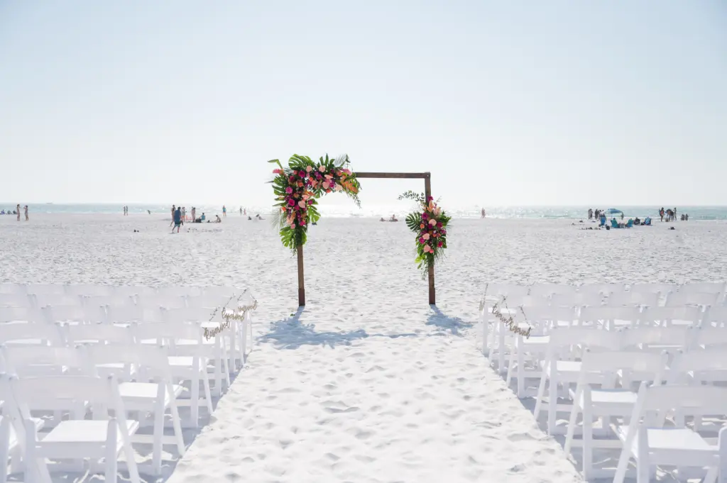 Beachfront Ceremony Inspiration with White Folding Chairs with Wooden Tropical Flowers Inspired Arch | Sarasota Planner MDP Events | Save the Date Florida