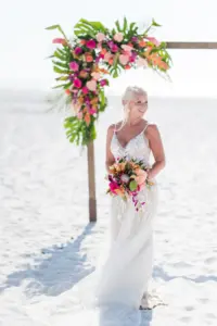 Bride in Front of Wooden Tropical Arch in Beach Wedding Ceremony with Bright Florals | St. Pete Wedding Florist Save the Date Florida | Photographer Amanda Zabrocki Photography