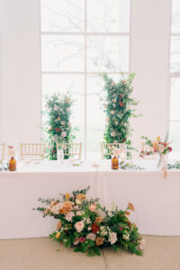 Asymmetrical Rose and Greenery Backdrop for Fall Garden Wedding Reception Head Table Inspiration | Bridal Party Feasting Table with Floor Flower Arrangement