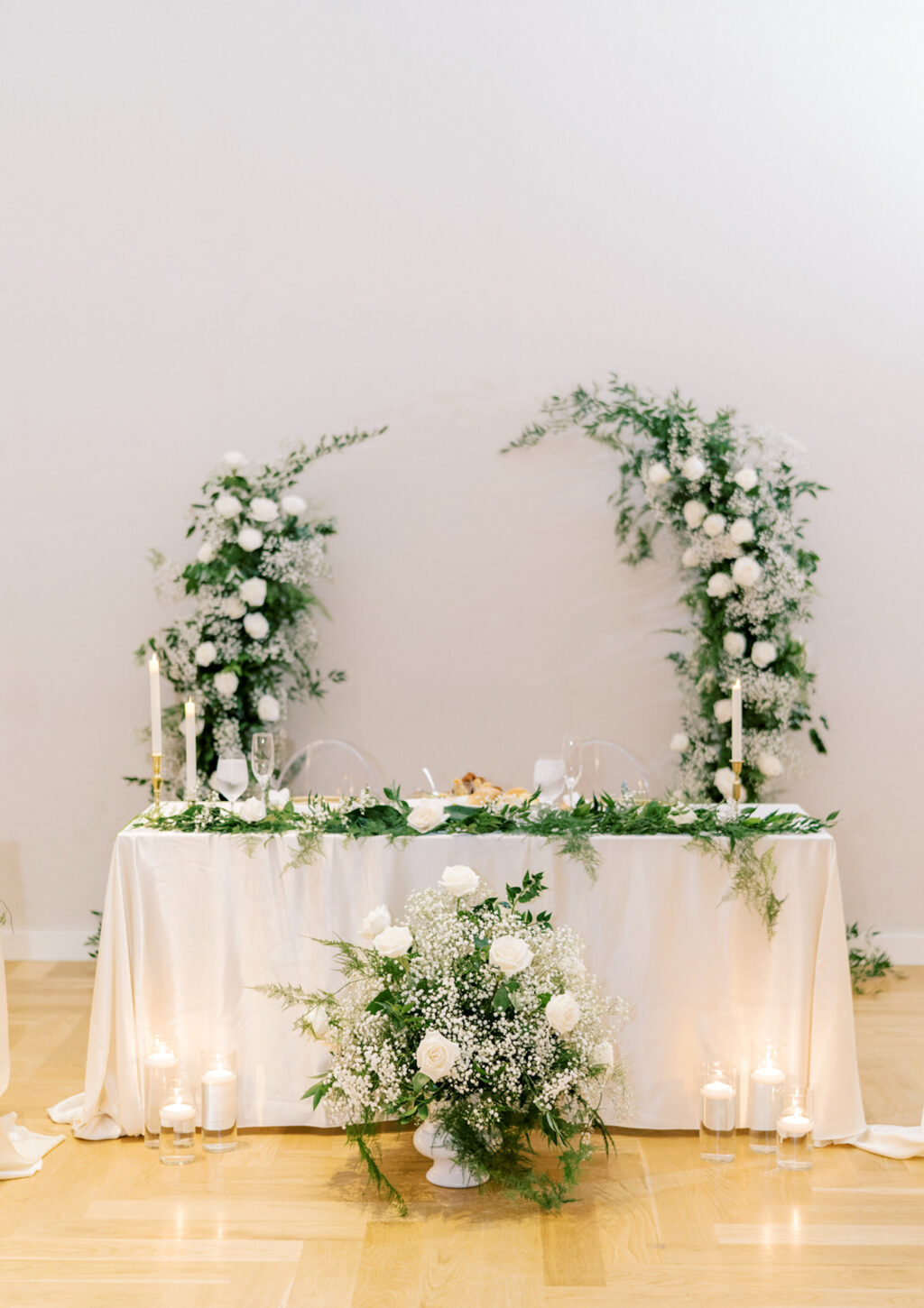 Wedding Reception Sweetheart Table Inspiration with Neutral Linen, Floating Candles and Greenery Garland | Asymmetrical Floral Backdrop with Baby's Breath and White Rose Ideas
