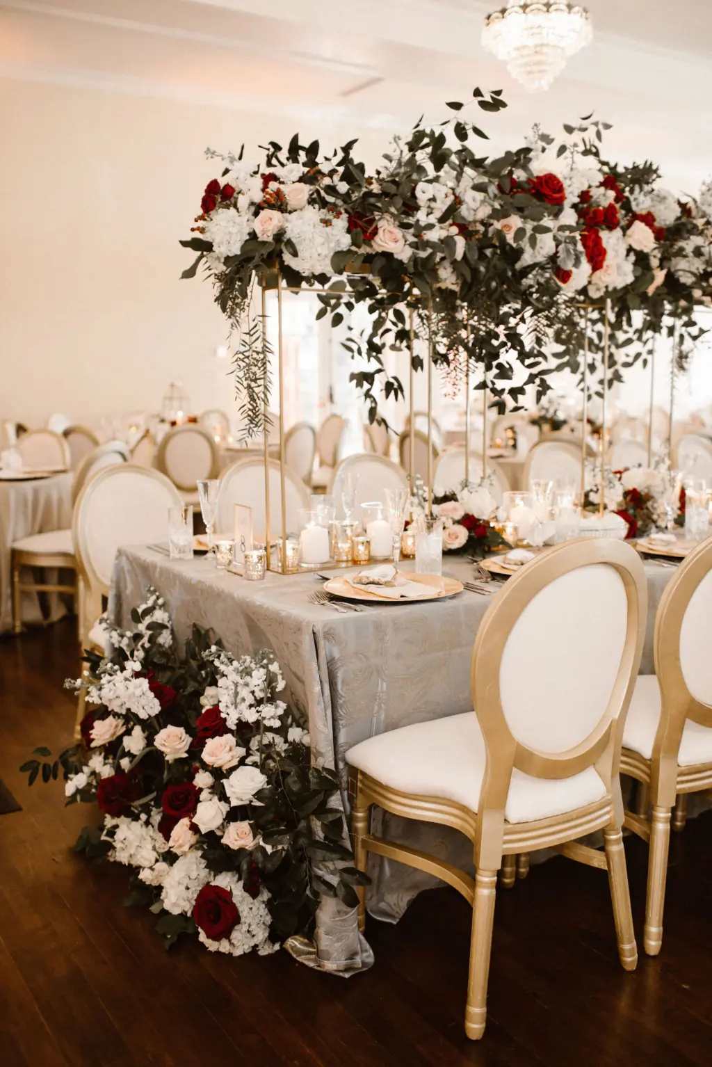 Tall Gold Flower Stand with Cascading Greenery, Burgundy, White, and Blush Rose Centerpiece Inspiration | Gold Chargers and Long Feasting Table for Wedding Reception