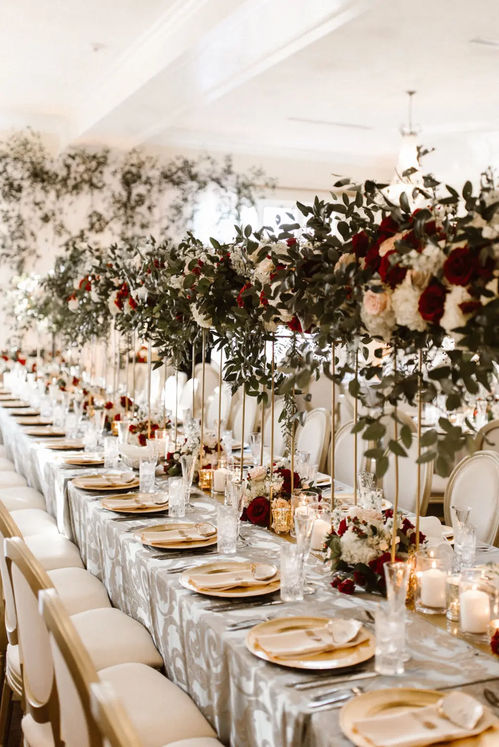 Tall Gold Flower Stand with Cascading Greenery, Burgundy, White, and Blush Rose Centerpiece Inspiration | Gold Chargers and Long Feasting Table for Wedding Reception | Tampa Bay Planner Unique Weddings and Events