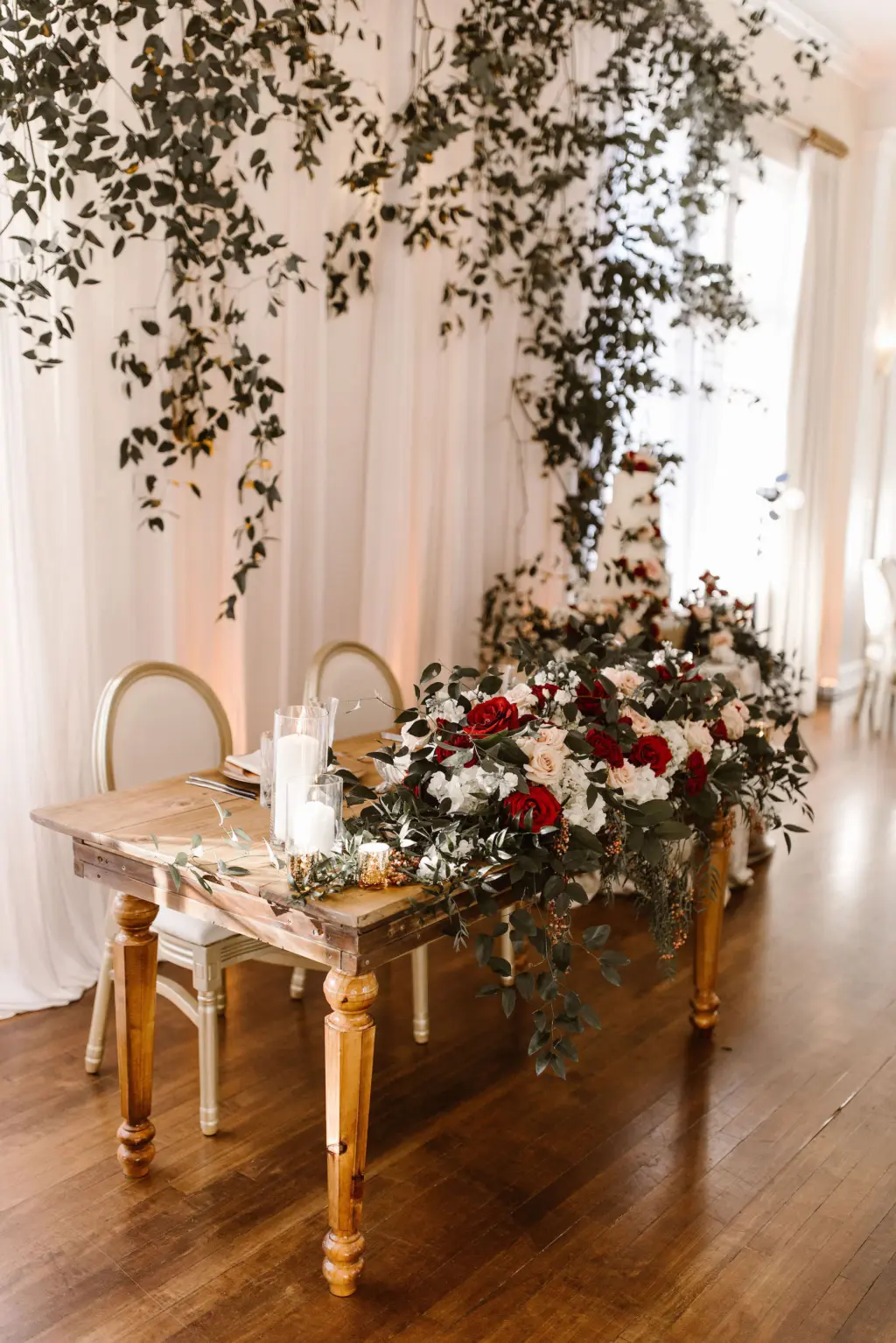 Cascading Greenery for Sweetheart Table at Wedding Reception with Extravagant Tabletop Burgundy and White Rose Flower Arrangement
