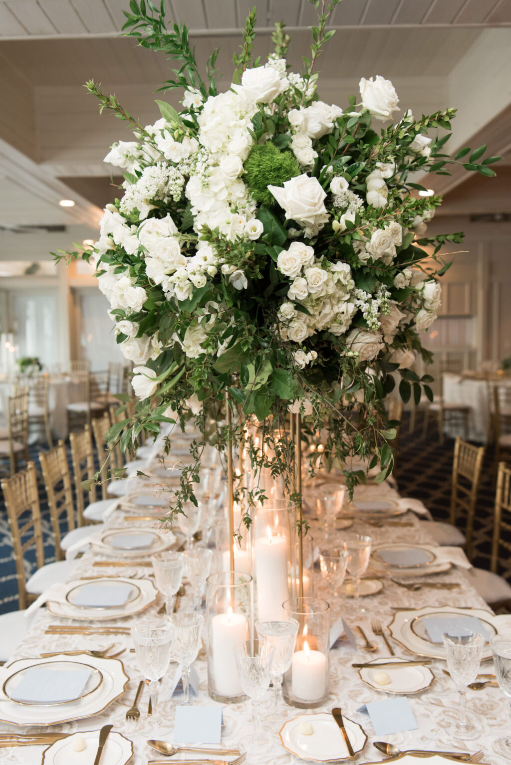 Tall Flower Stand with White Roses, Babies Breath, and Greenery Centerpiece for Wedding Reception Inspiration | Long Feasting Tables with Gold and White Table Settings | Tampa Bay Rentals A Chair Affair | Kate Ryan Event Rentals
