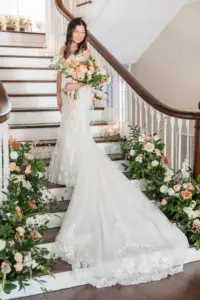 Bride in Long Train Lace Wedding Gown with Peach, Orange, Blush, Cream Floral Wedding Bouquet with Greenery Details on Staircase Bridal Wedding Portrait | Tampa Wedding Photographer Mary Anna Photography | Venue The Orlo | Hair and Makeup Femme Akoi Beauty Studio