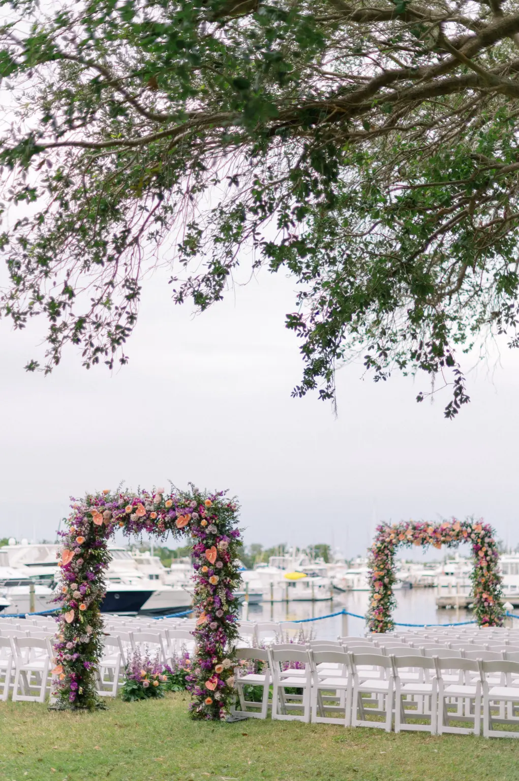 Tropical Floral Aisle Arch Inspiration | Orange Anthurium, Pink Roses, Purple Foxglove Flowers, and Greenery | Waterfront Wedding Ceremony Ideas | Folding Garden Chairs | Sarasota Florist Botanica International Design Studio