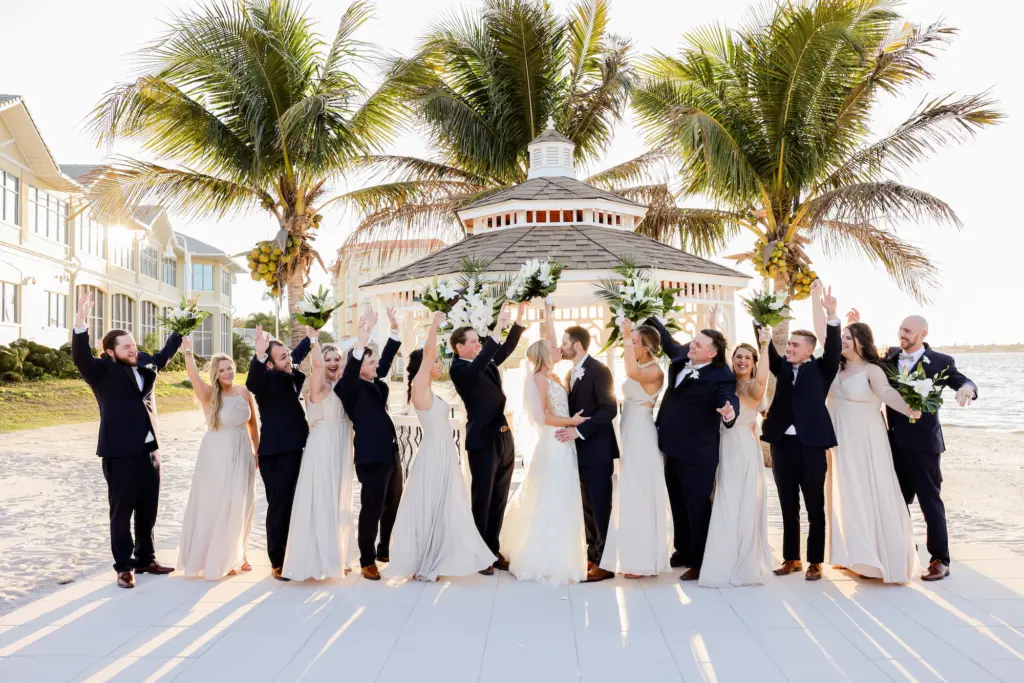 Bride and Groom with Wedding Party On Beach | Navy Three-piece Tuxedo Ideas | Champagne Mismatched Bridesmaids Dresses Inspiration | Tampa Bay Photographer Lifelong Photography | Videographer Shannon Kelly Films | Planner Coastal Coordinating | Venue Isla del Sol Yacht Club